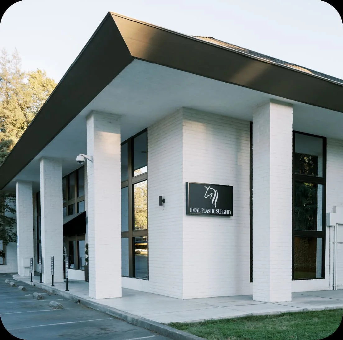QUIENES-SOMOS Exterior of a white modern clinic with large glass windows and a sign reading 'Ideal Plastic Surgery' with a logo.